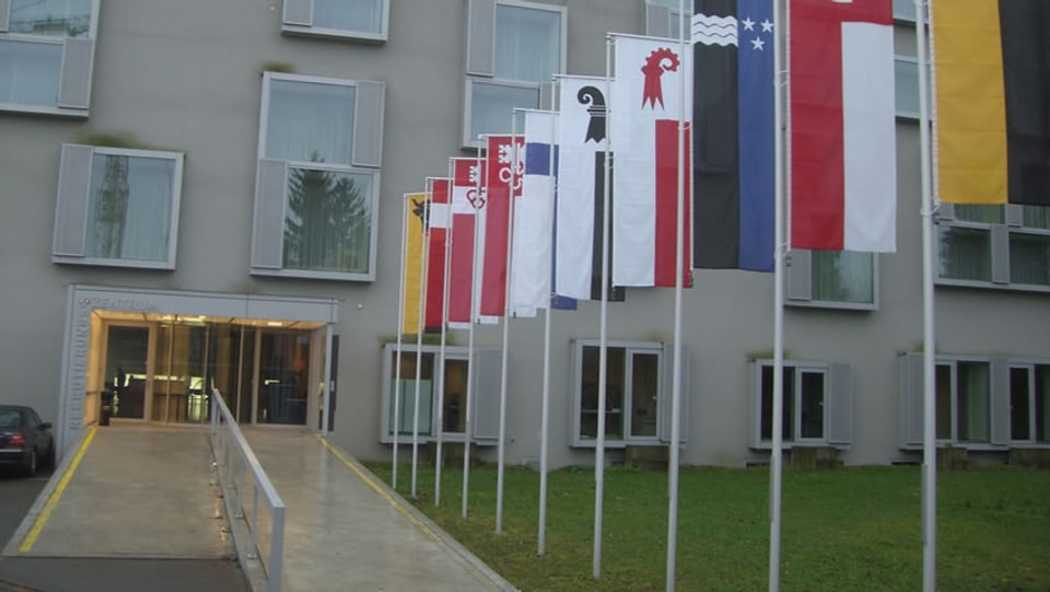 Das Rekrutierungszentrum von Windisch von aussen, mit diversen Kantonsfahnen neben dem Gehweg.