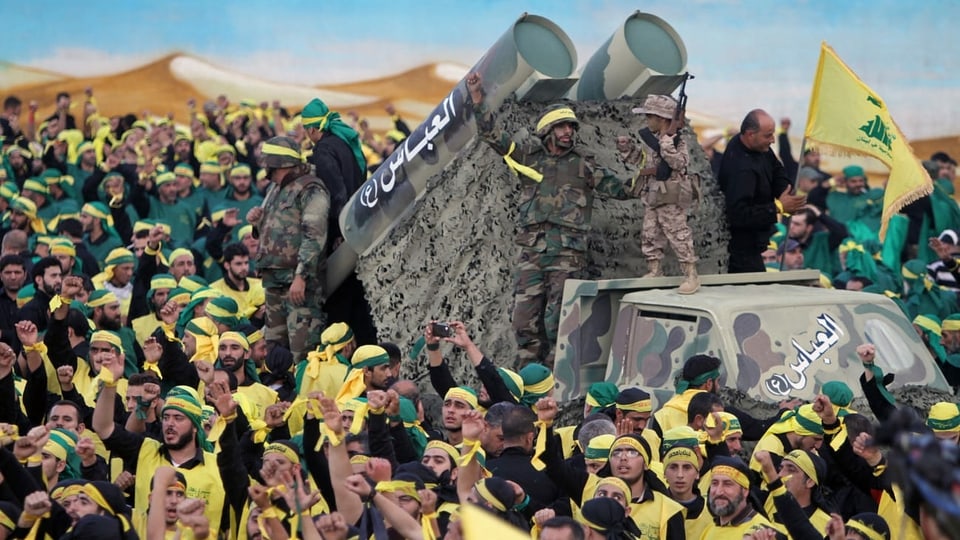 Männer in gelben Hisbollah-Shirts, auf einem Fahrzeut zwei Raketenwerfer.