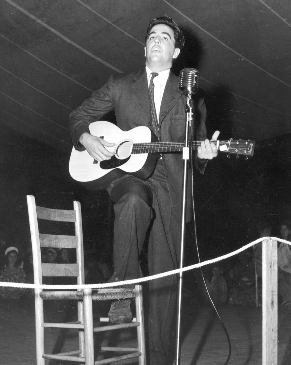 Schwarzweissfoto: Lomax mit Gitarre auf einer Bühne.