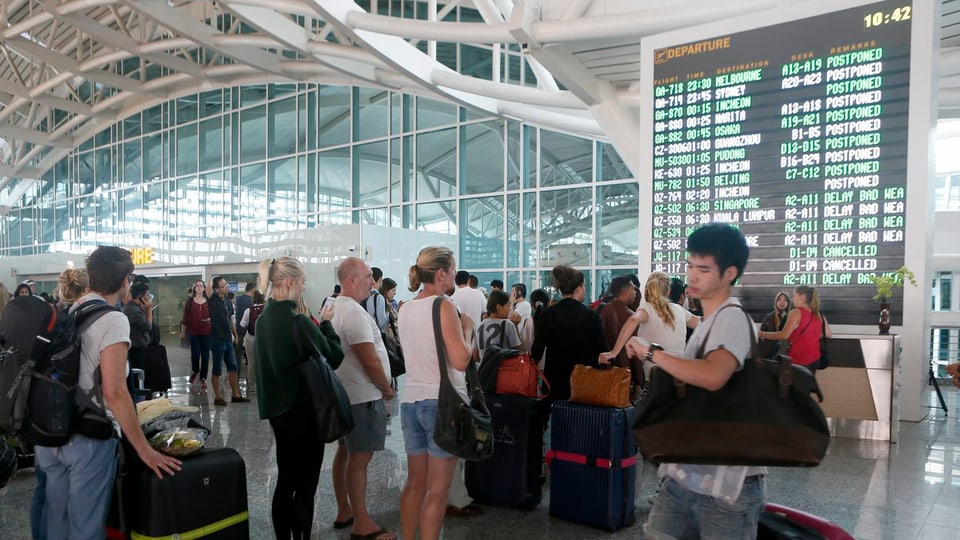 Passagiere vor einer Informationsrafel am internationalen Flughafen von Bali.