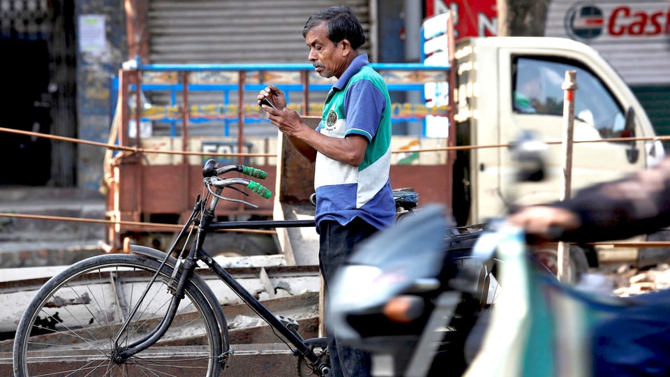 Inder mit Fahhrad am Strassenrand, in den Händen hält er ein Smartphone.