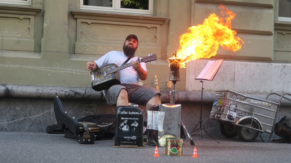 Ein Mann spielt Gitarre, vor ihm brennt eine Kaffeekanne.