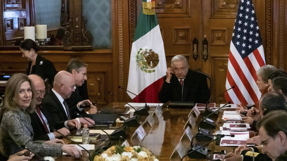 Menschen rund um einen Tisch. Dahinter die Flaggen von Mexiko und den USA.