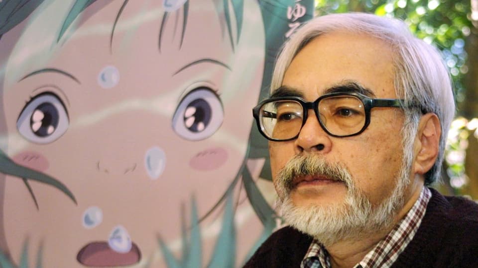 Ein älterer Mann mit Brille und Bart schaut nachdenklich. Im Hintergrund eine Zeichentrick-Zeichnung.