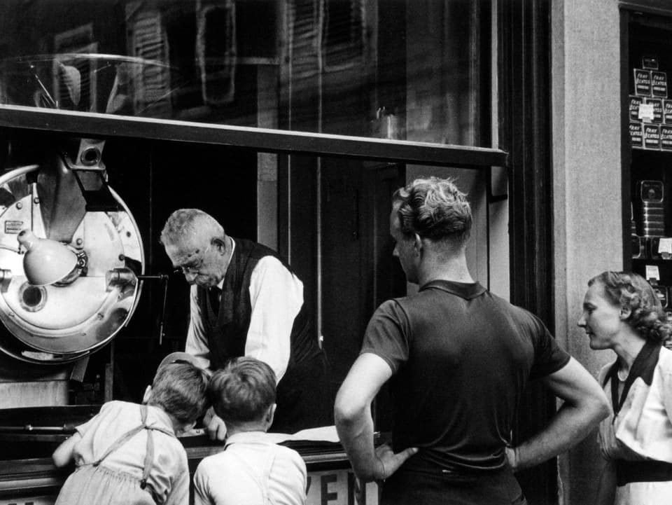 Zwei Buben und ihre Eltern schauen durch das geöffnete Fenster Heinrich II. Schwarzenbach beim Kaffeerösten zu.
