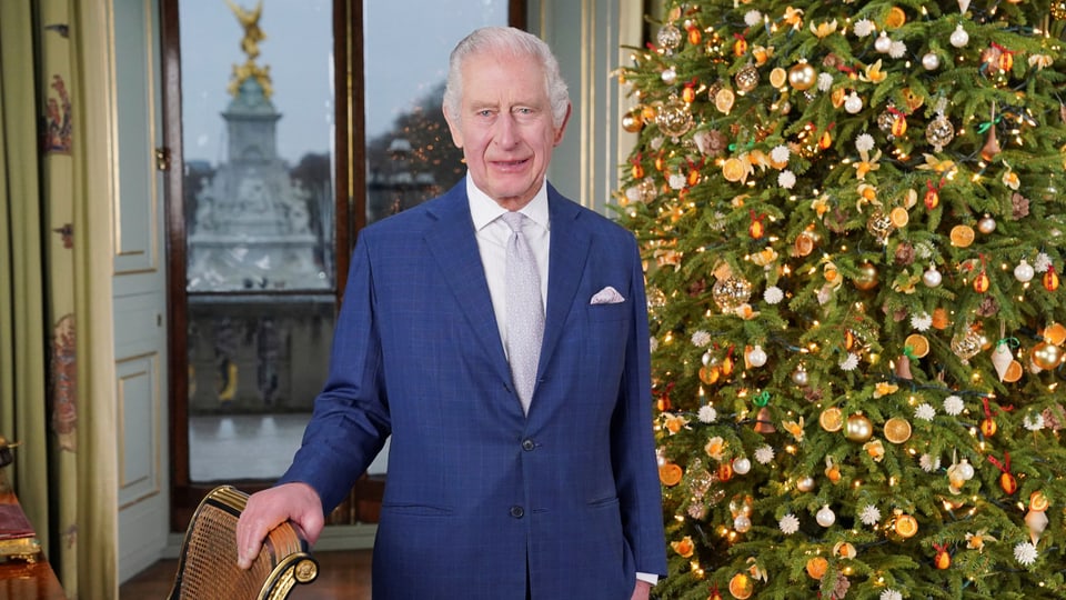 König Charles III. steht vor einem geschmückten Weihnachtsbaum.