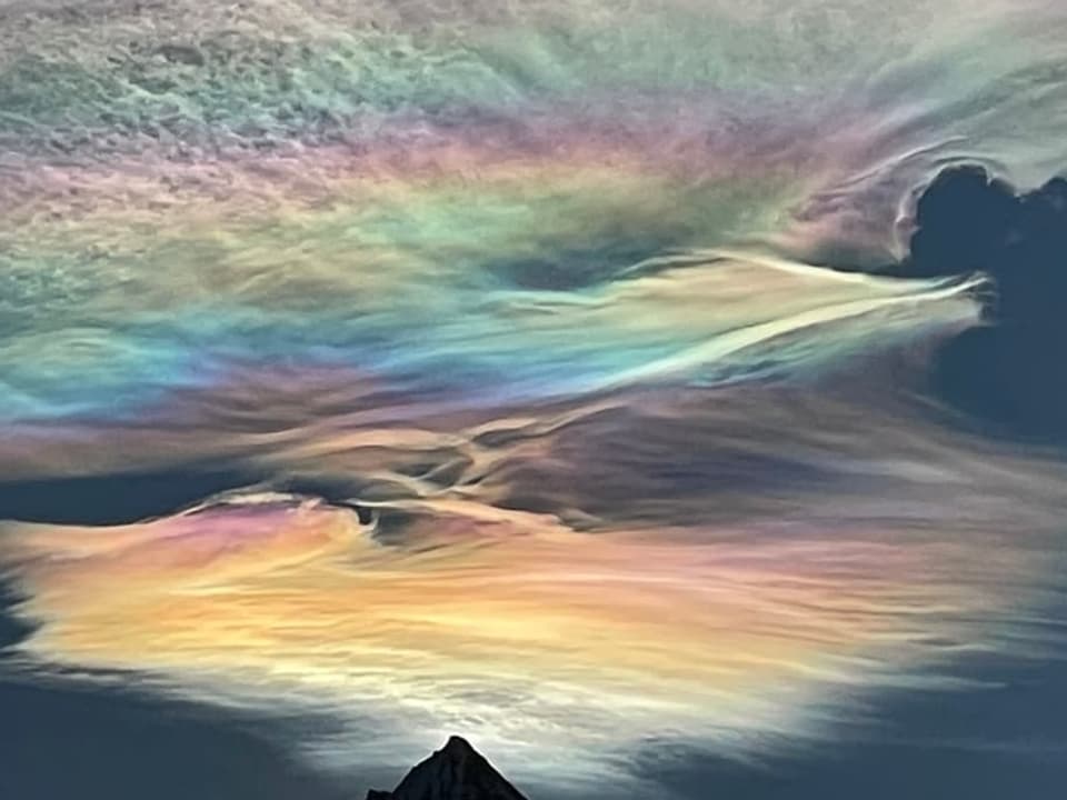 Himmel mit dünnen hohen Wolkenfeldern, die in allen Regenbogenfarben leuchten. 