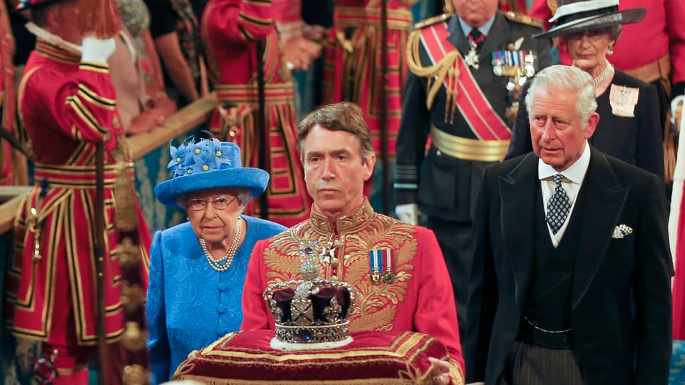 Queen geht neben ihren Sohn im Parlament. Vor ihr trägt ein Uniformierter die Krone.