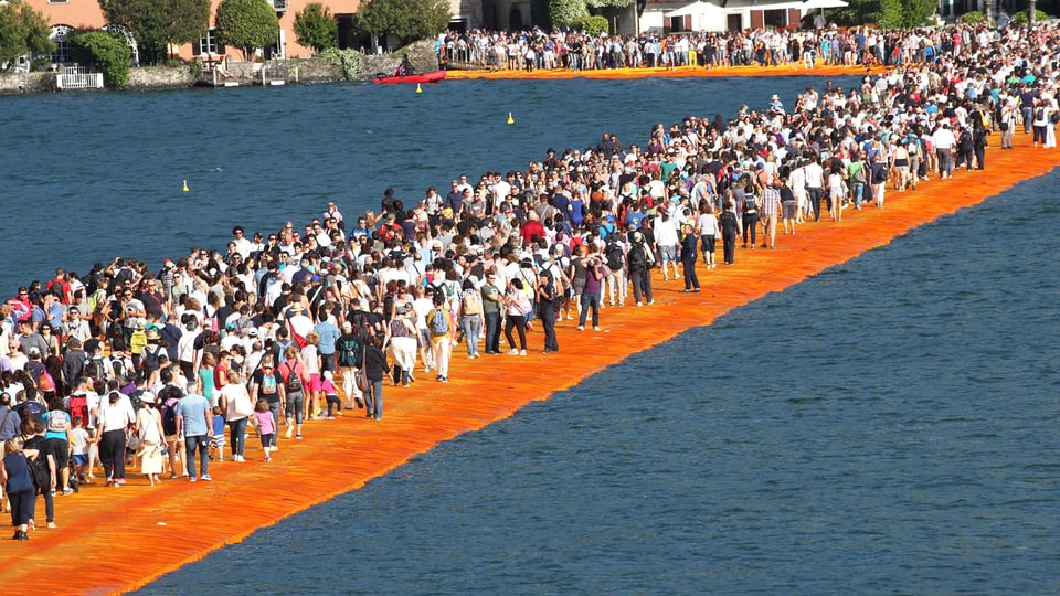 Eine Menschenmasse geht über einen breiten Steg auf einem See.