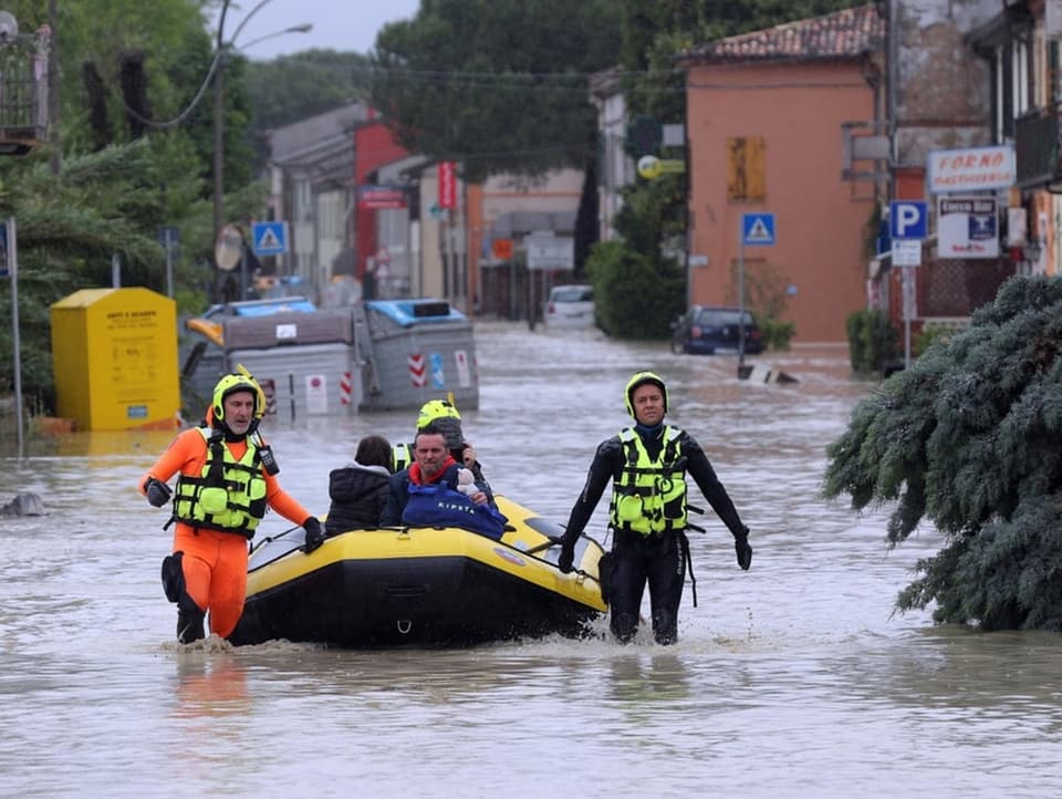 Menschen in Boot auf überfluteter Strasse.