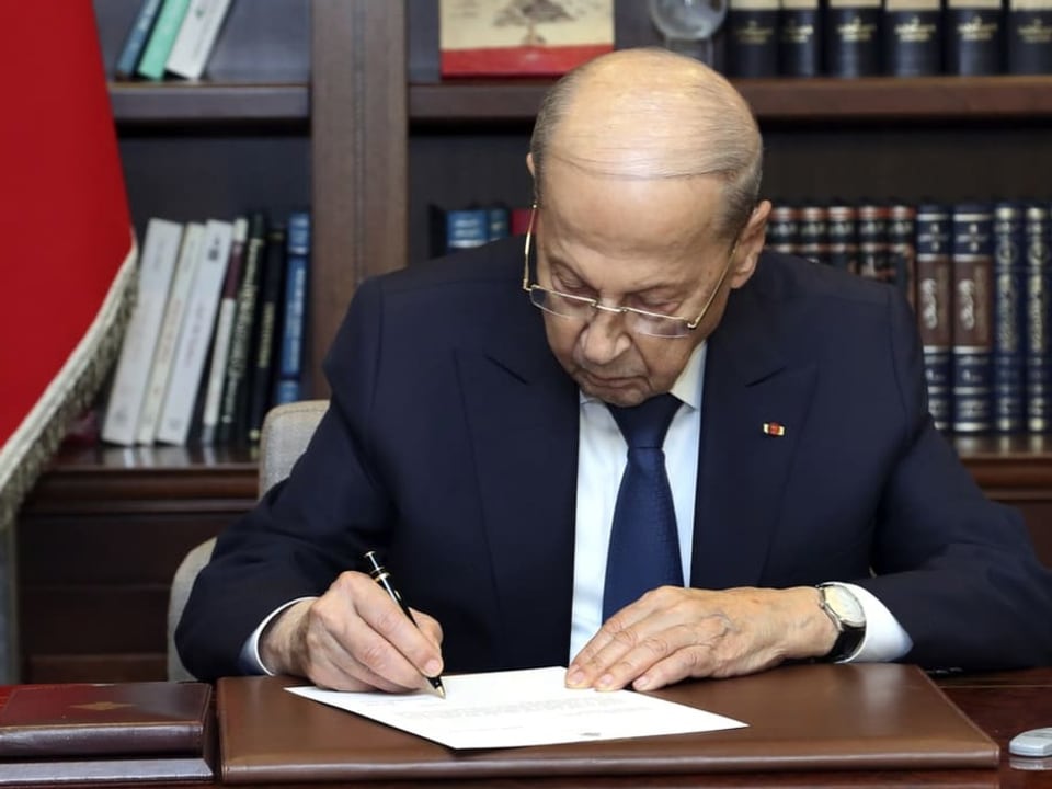 Aoun unterschreibt ein Dokument auf einen Schreibtisch.