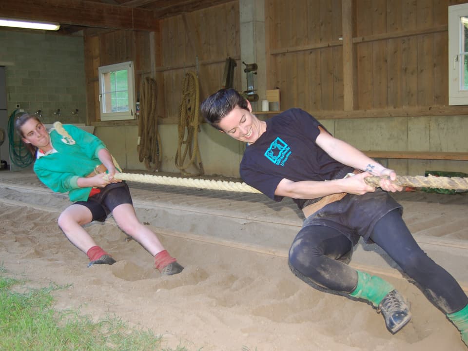 Zwei junge Frauen stemmen sich mit den Füssen in den Sand und ziehen kräftig an einem Seil.