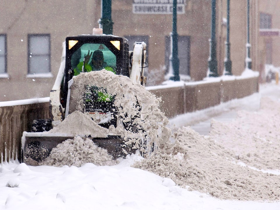 Eine Schneefräse räumt einen Gehsteig in einem Ort in Milwaukee USA. Er macht das Victory-Zeichen.