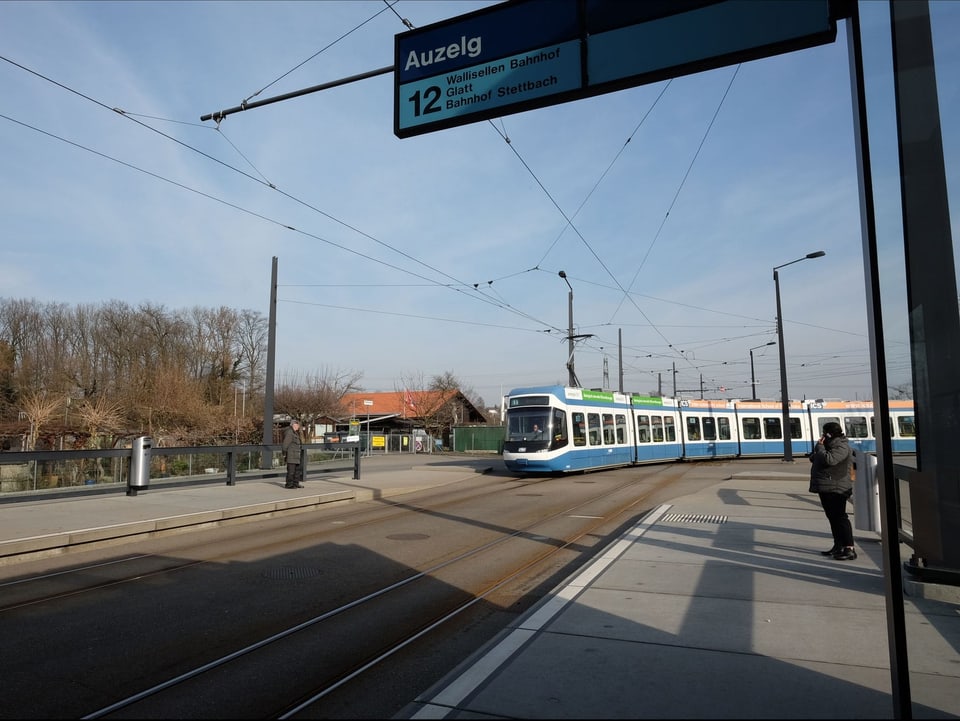 Ein blau-weisses Tram an der Endstation, linkerhand sieht man Schrebergärten.