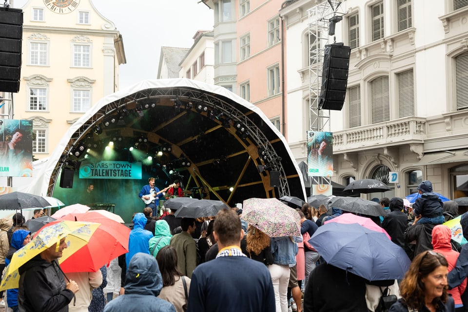 Menschen unter Regenschirmen vor der Konzertbühne.