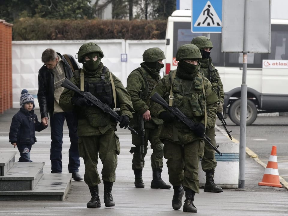 Eine Gruppe vermummter und bewaffneter Männer wieder auf dem Flughafen von Simferopol. Dahinter ein kleiner Junge, der seinem Vater gerade die Hand geben will.  
