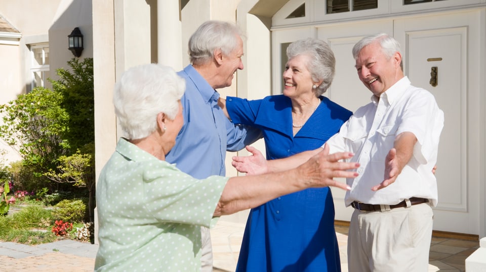 Zwei Seniorenpärchen begrüssen sich vor einem Hauseingang.
