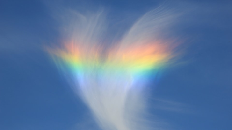 Eine Schleierwolke durch die ein grosses regenbogenfarbenes Band läuft.