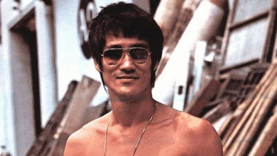 Nahaufnahme von Bruce Lee mit Sonnenbrille und nacktem Oberkörper.