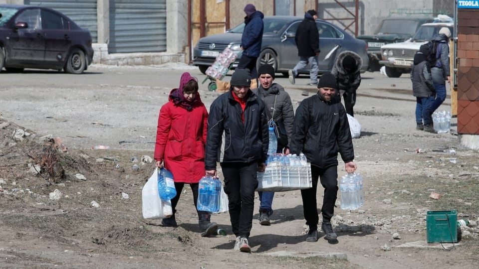 Menschen in der belagerten Stadt Mariupol tragen Wasserflaschen.