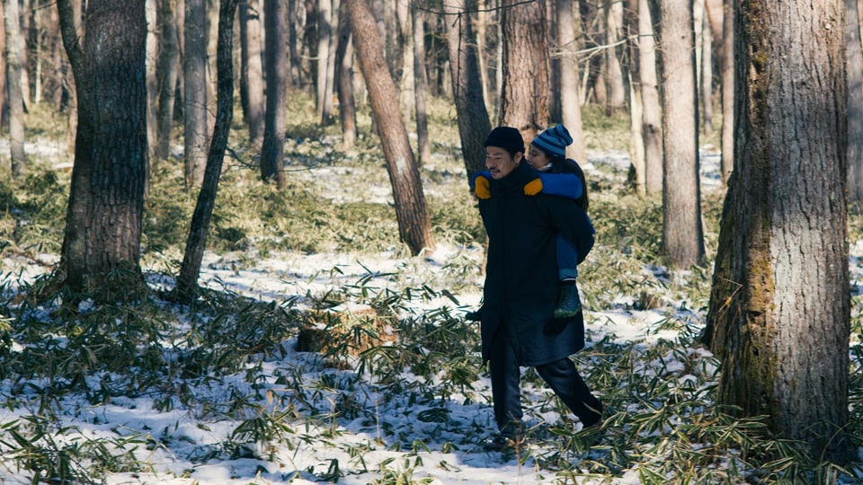 In einem verschneiten Wald trägt ein Mann ein junges Mädchen auf seinem Rücken