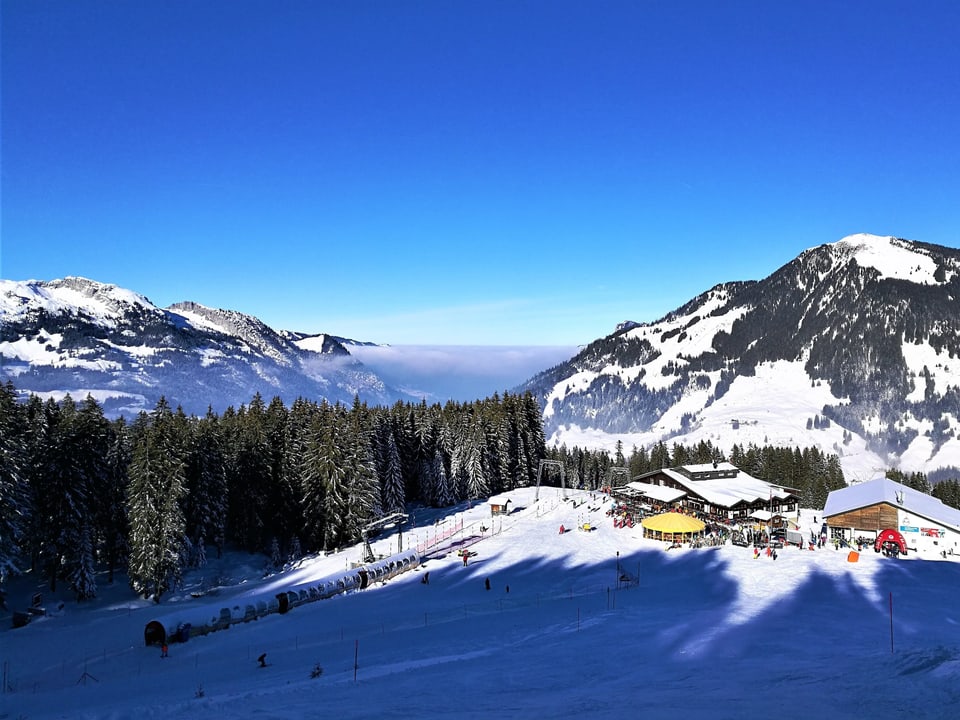 Auf dem Bild sieht man die Rossweid mit dem Bergrestaurant. Im Hintergrund das Nebelmeer und darüber blauer Himmel.