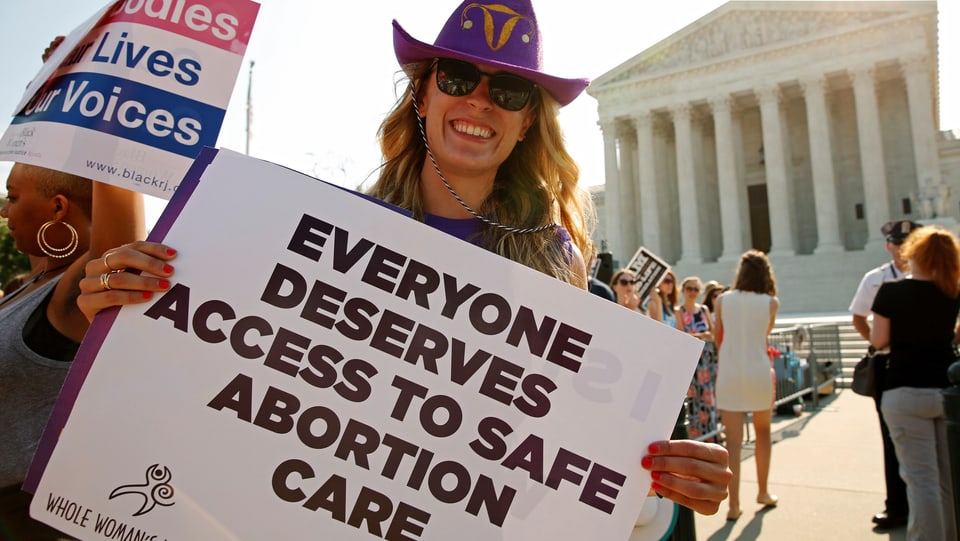 Eine Frau mit einem Plakat, auf dem "Everyone Deserves Access to Safe Abortion Care"