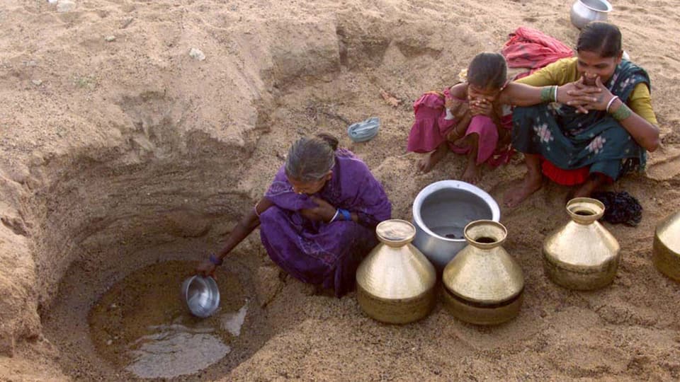 Drei Frauen hocken im ausgetrockneten Flussbett und schöpfen Wasser aus einem kleinen Loch.
