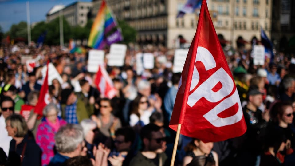 Menschenmenge bei einer Demonstration mit einer SPD-Flagge im Vordergrund.