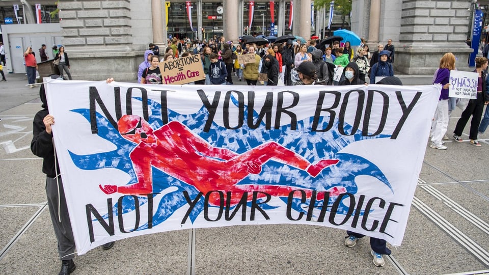 Mehrere Menschen halten ein grosses Banner, auf dem steht: «Not your body, not your choice.»