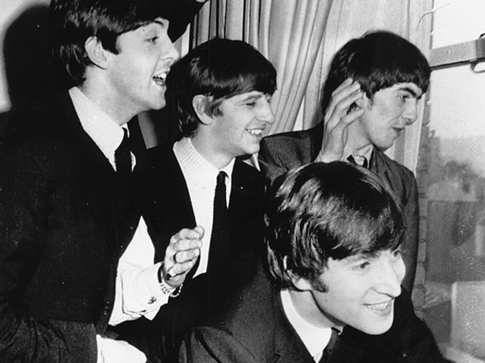 Die Beatles 1964 an einem Fenster.