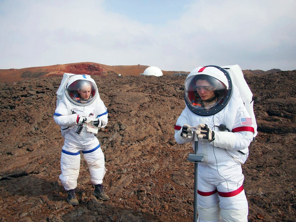 Zwei Forscher im Raumanzug auf der Vulkanoberfläche.