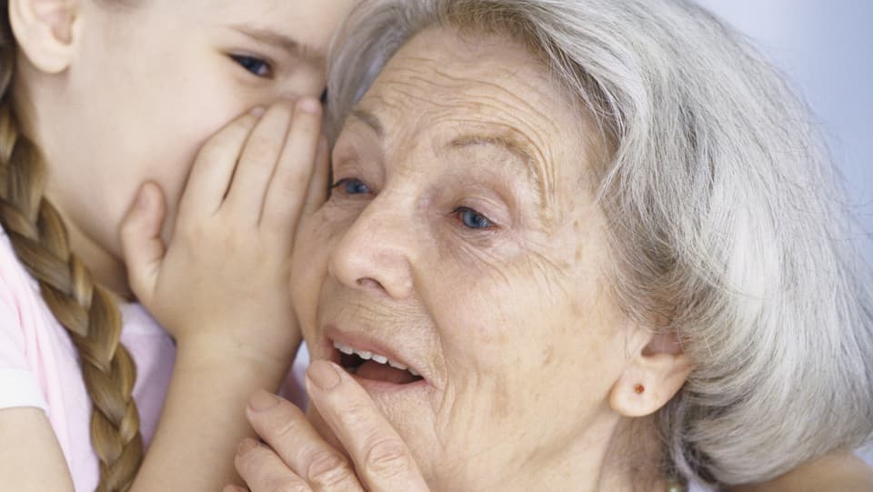 Ein Kind flüstert einer älteren Frau ins Ohr.
