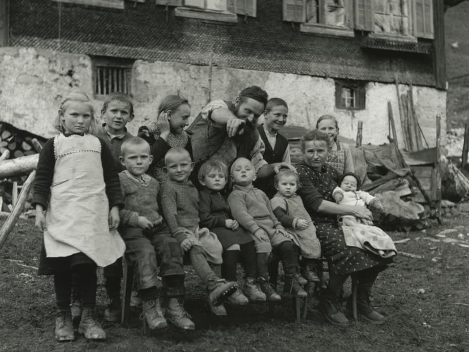 Schwarz-Weiss-Bild: Eine (Bauern-)Grossfamilie posiert vor dem Haus in zwei Reihen.