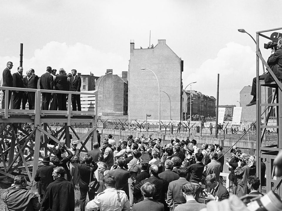 Kennedy steht auf einem Podest bei der Berliner Mauer.