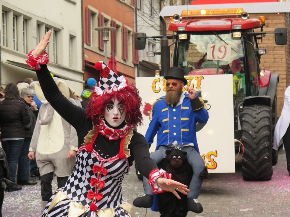 Clownin vor Traktor mit Umzugwagen