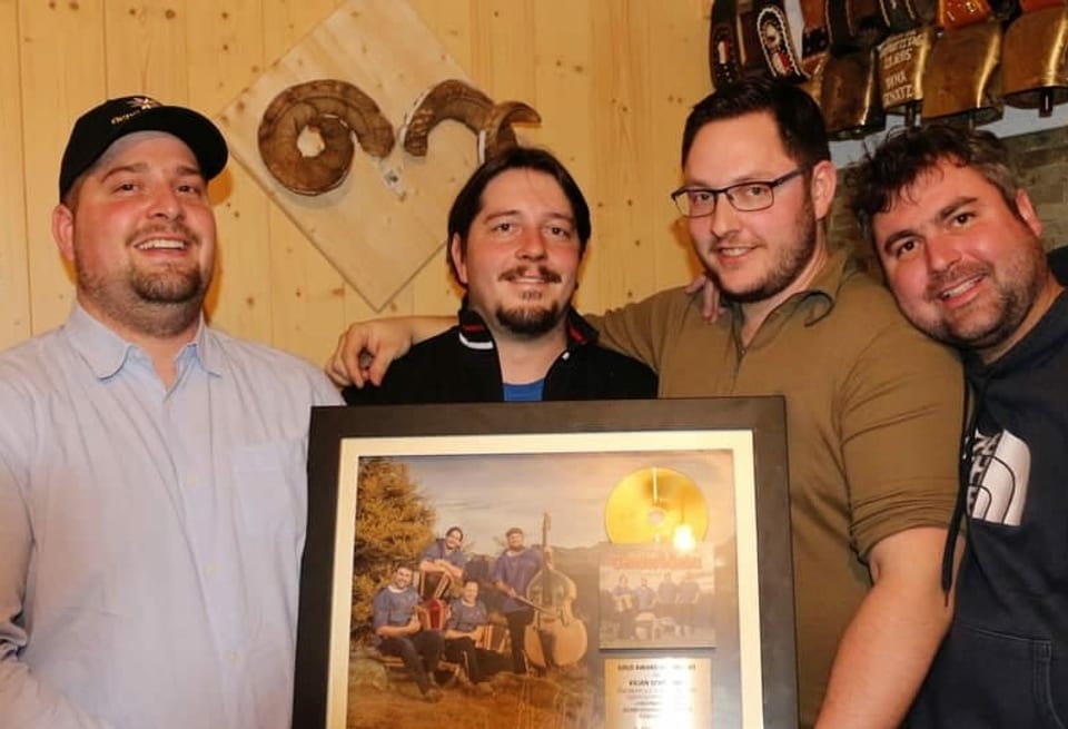 Vier Männer halten eingerahmte Goldene Schallplatte in Händen. 