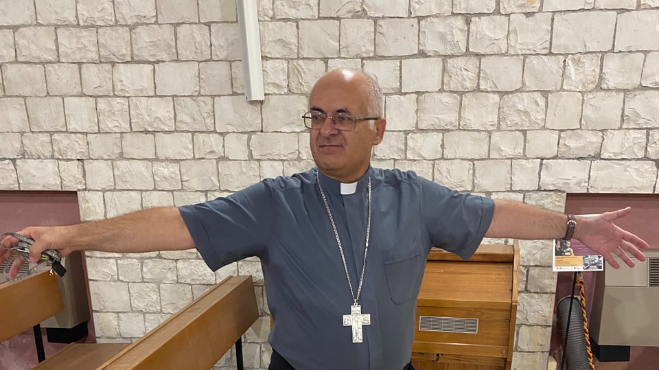 Ein kahlköpfiger Priester breitet die Arme aus