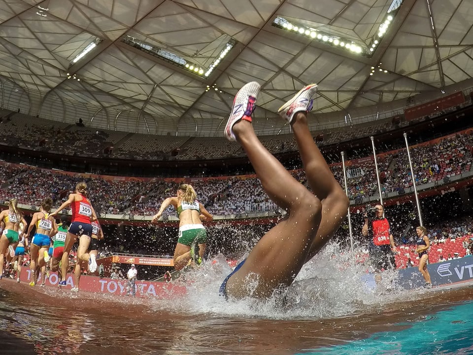 Rolanda Bell stürzt kopfüber in den Wassergraben, ihre Konkurrentinnen laufen im Hintergrund weiter.