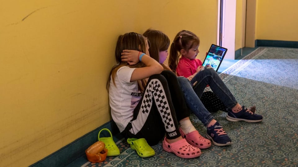 Drei ukrainische Mädchen sitzen am Boden und spielen mit einem Tablet.