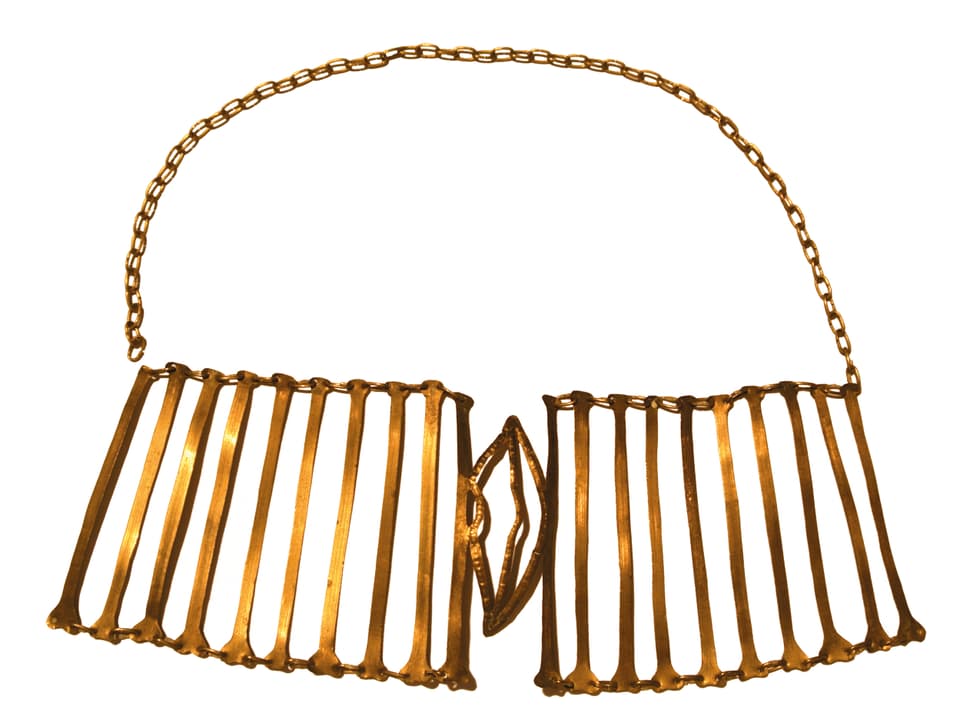 Grosse, goldene Halskette, in deren Mitte sich ein Mund aus Metall befindet.
