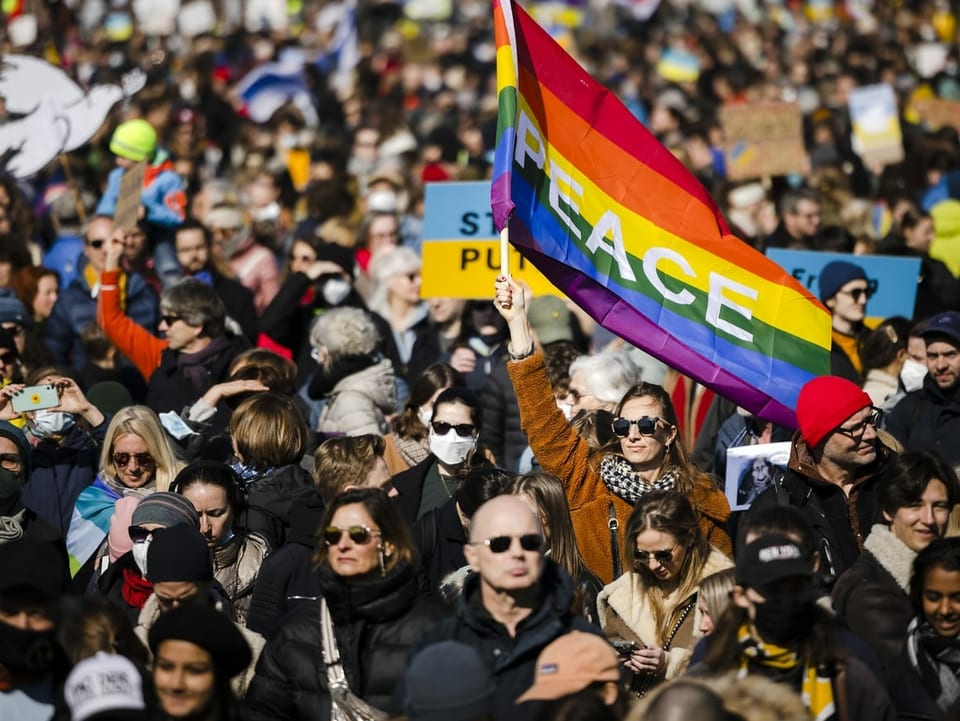 Tausende Demonstrierende auf der Strasse. Im Zentrum weht eine Person mit einer «Peace»-Fahne.