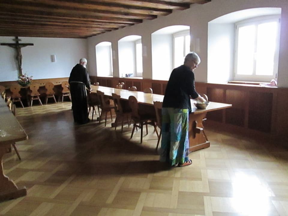 Ein Mann in Mönchskutte und eine Frau im Speisesaal des Klosters.