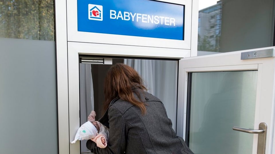 Eine Frau legt eine Pupe ins Babyfenster.