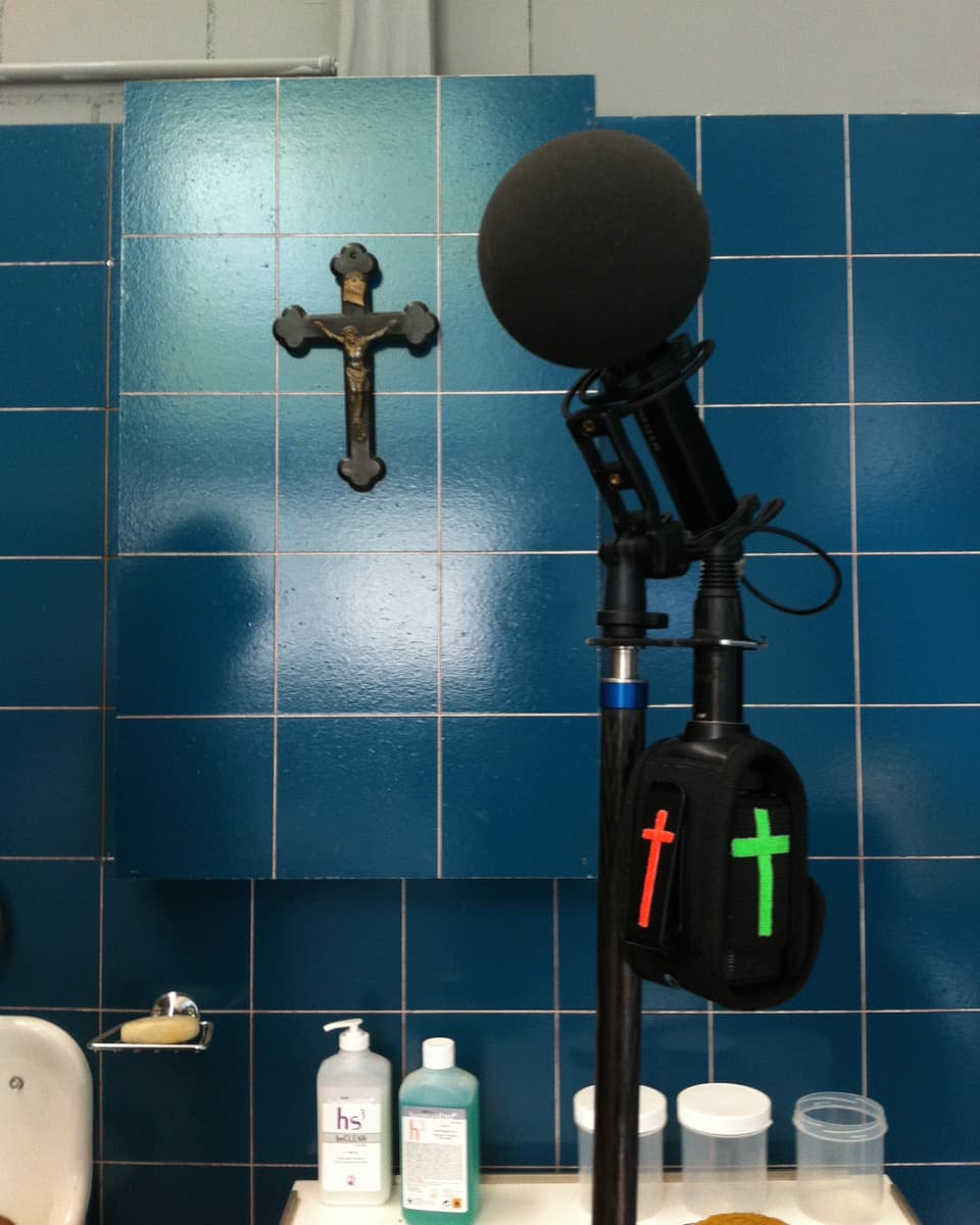 Mikrofon vor blau gekachelter Wand. Auf dem angehängten Sender sind mit buntem Klebeband Kreuze angebracht.