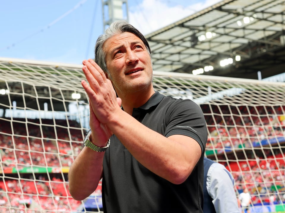 Man in black shirt claps in front of football goal.