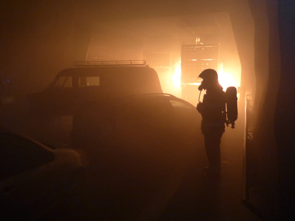 Feuer im Hintergrund, Mann in Feuerwehr-Montour im Vordergrund. 