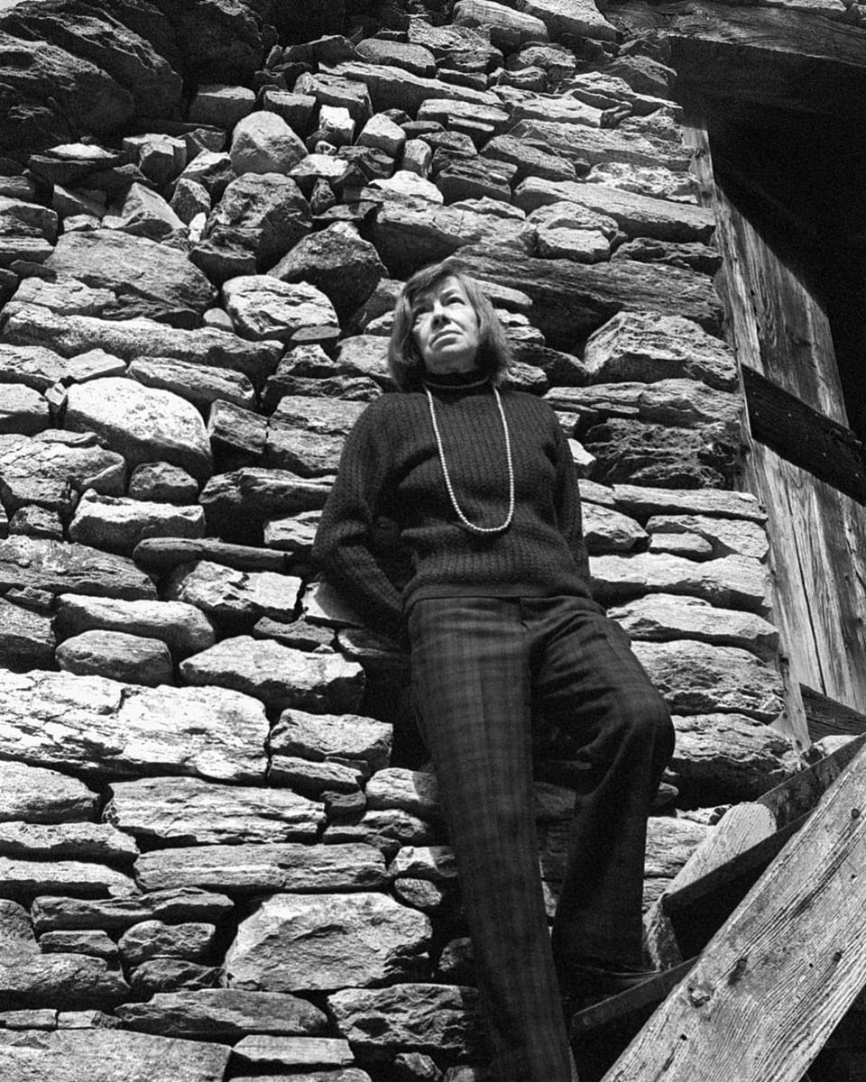 schwarzweiss Bild ältere Frau steht vor Steinwand, angelehnt.