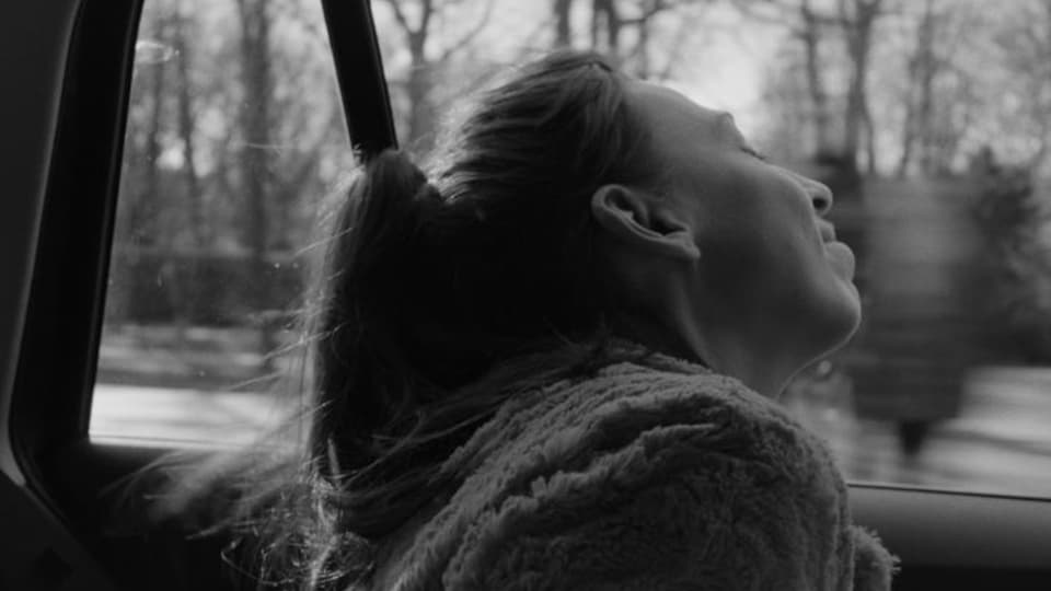 In a scene from Cosima Frei's black and white short film, Carol Schuler looks out the window in a taxi.