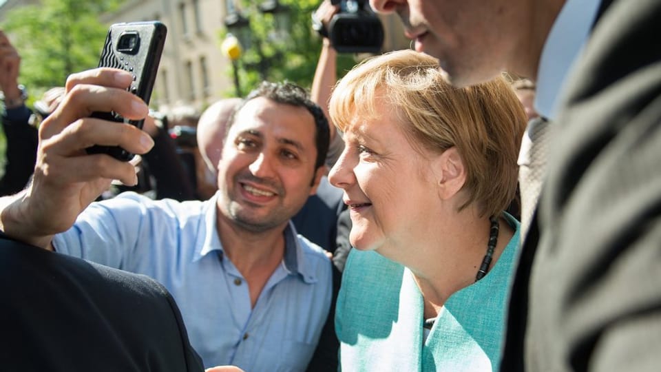 Angela Merkel macht mit einem Flüchtling ein Selfie.